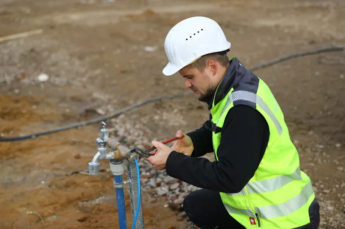 Bauarbeiter in Warnweste schließt temporären Wasseranschluss auf Baustelle an