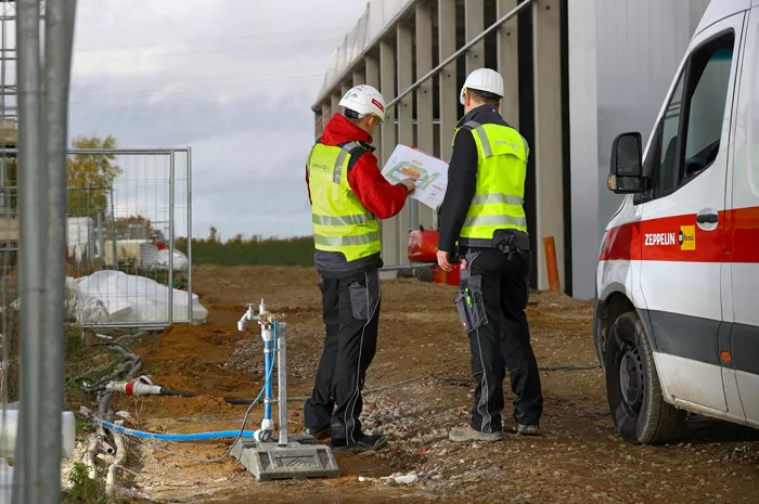 Zwei Bauarbeiter in Sicherheitskleidung planen temporäre Bauwasserversorgung an Baustelle mit Hydrantenanschluss