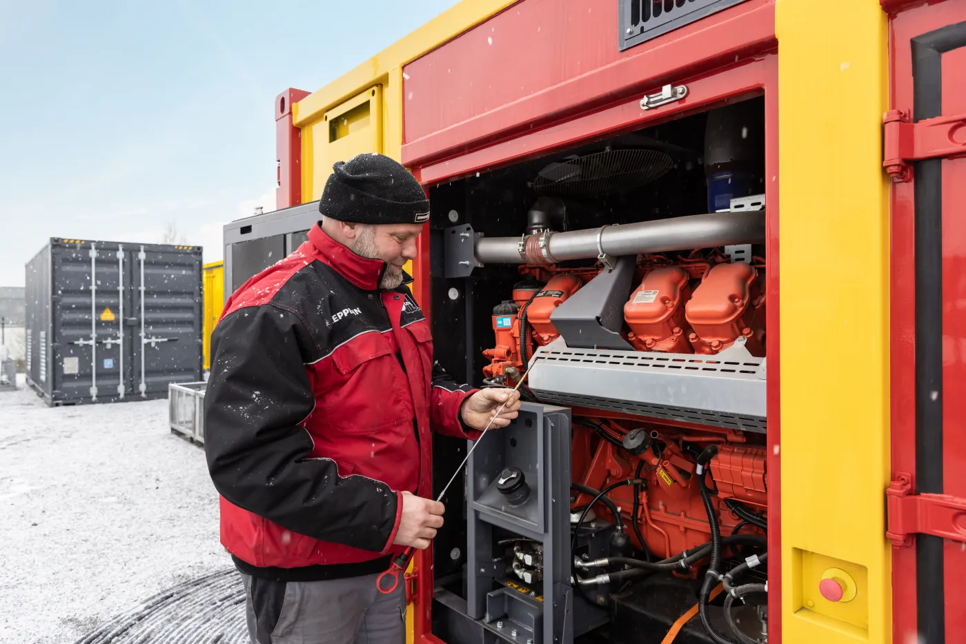 Servicemitarbeiter prüft Ölstand an Notstromaggregat von Zeppelin Rental auf verschneitem Betriebsgelände