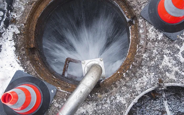 Wasser strömt aus Rohrleitung in geöffneten Kanalschacht, umgeben von Warnkegeln