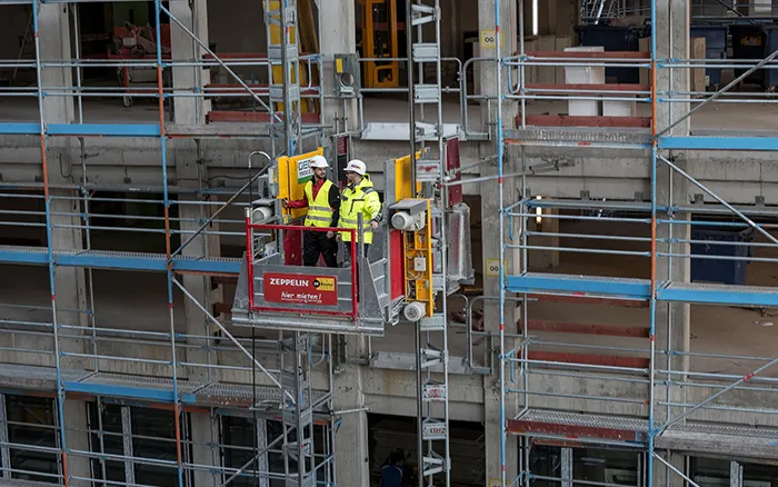 Zwei Bauarbeiter in einer Hebebühne bei Sicherheitsbegehung an einem Baugerüst