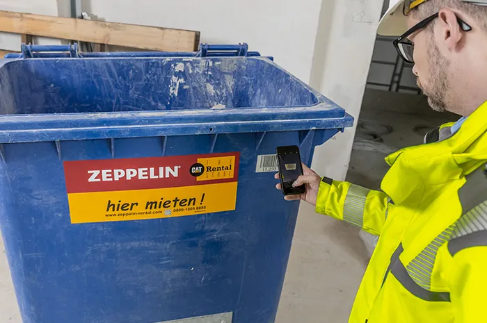 Bauarbeiter scannt mit Smartphone einen Container von Zeppelin Rental zur digitalen Entsorgungsdokumentation
