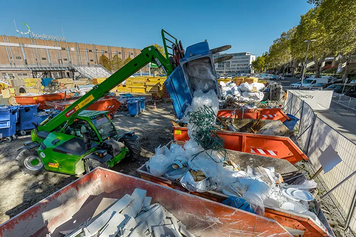 Teleskoplader entleert Baustellenmüll in Container auf Entsorgungsfläche