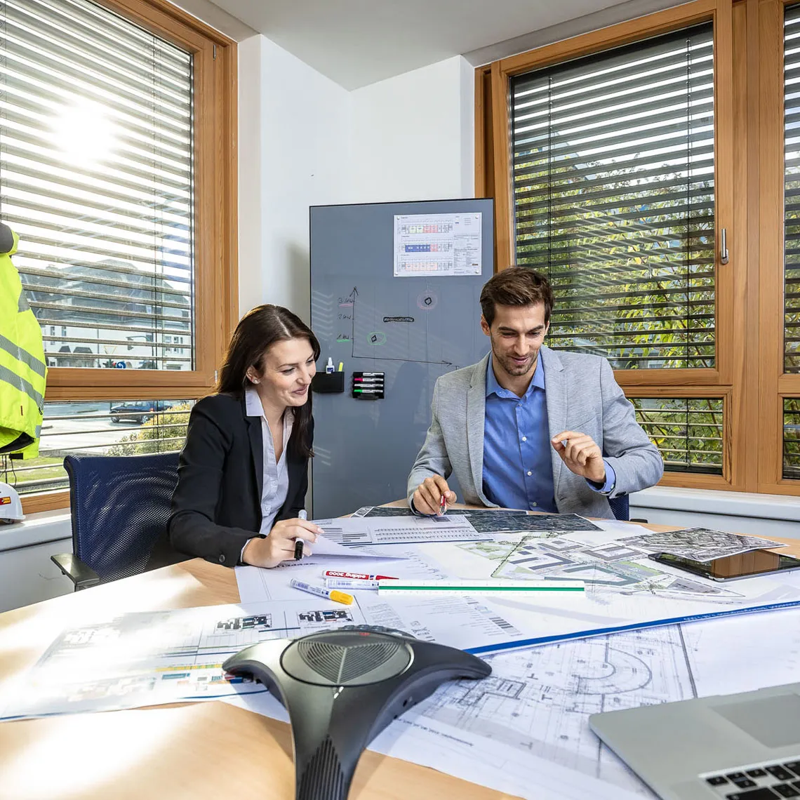 Zwei Projektplaner im Büro besprechen Baupläne und Logistikkonzepte für eine Baustelle