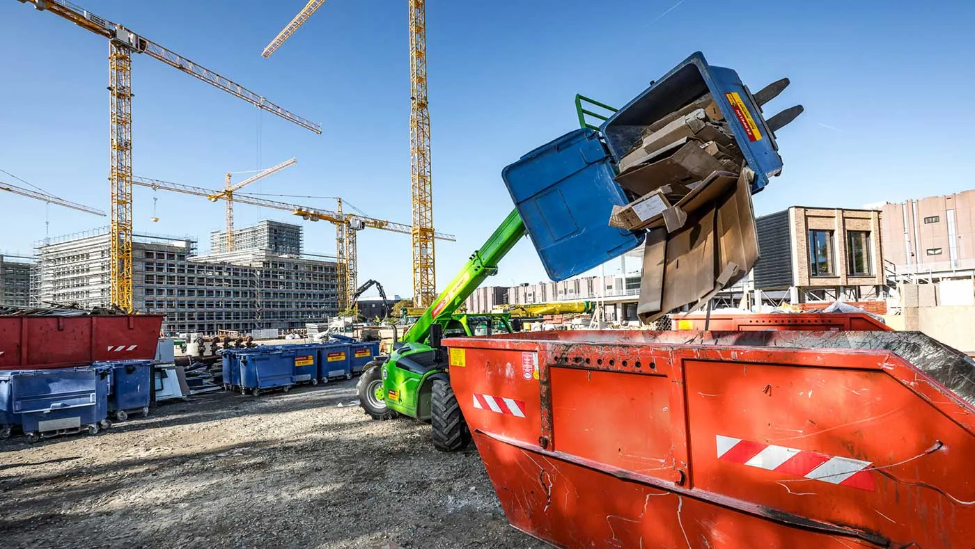 Teleskoplader leert Baustellenabfall in Container auf Großbaustelle mit mehreren Kränen im Hintergrund