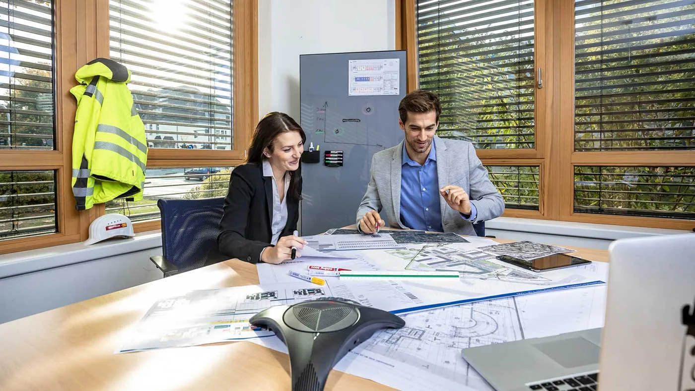 Zwei Projektplaner im Büro besprechen Baupläne und Logistikkonzepte für eine Baustelle