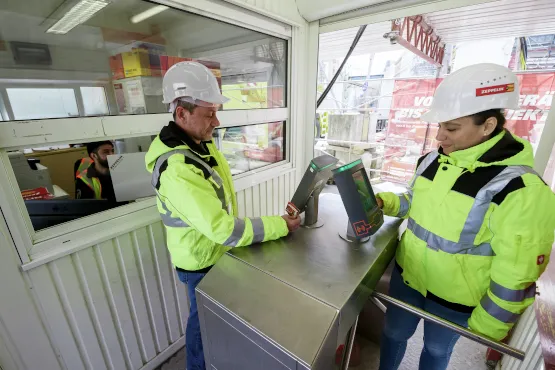 Zwei Bauarbeiter scannen ihre Ausweise an Zutrittskontrollsystem auf Baustelle
